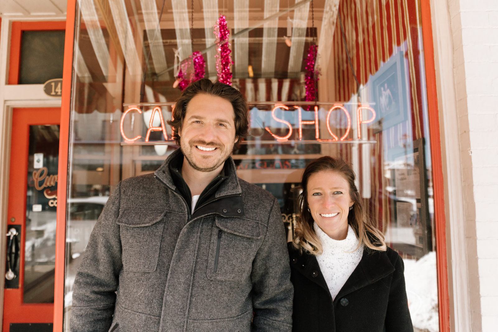 winter engagement session happy couple smiling neon sign coffee shop